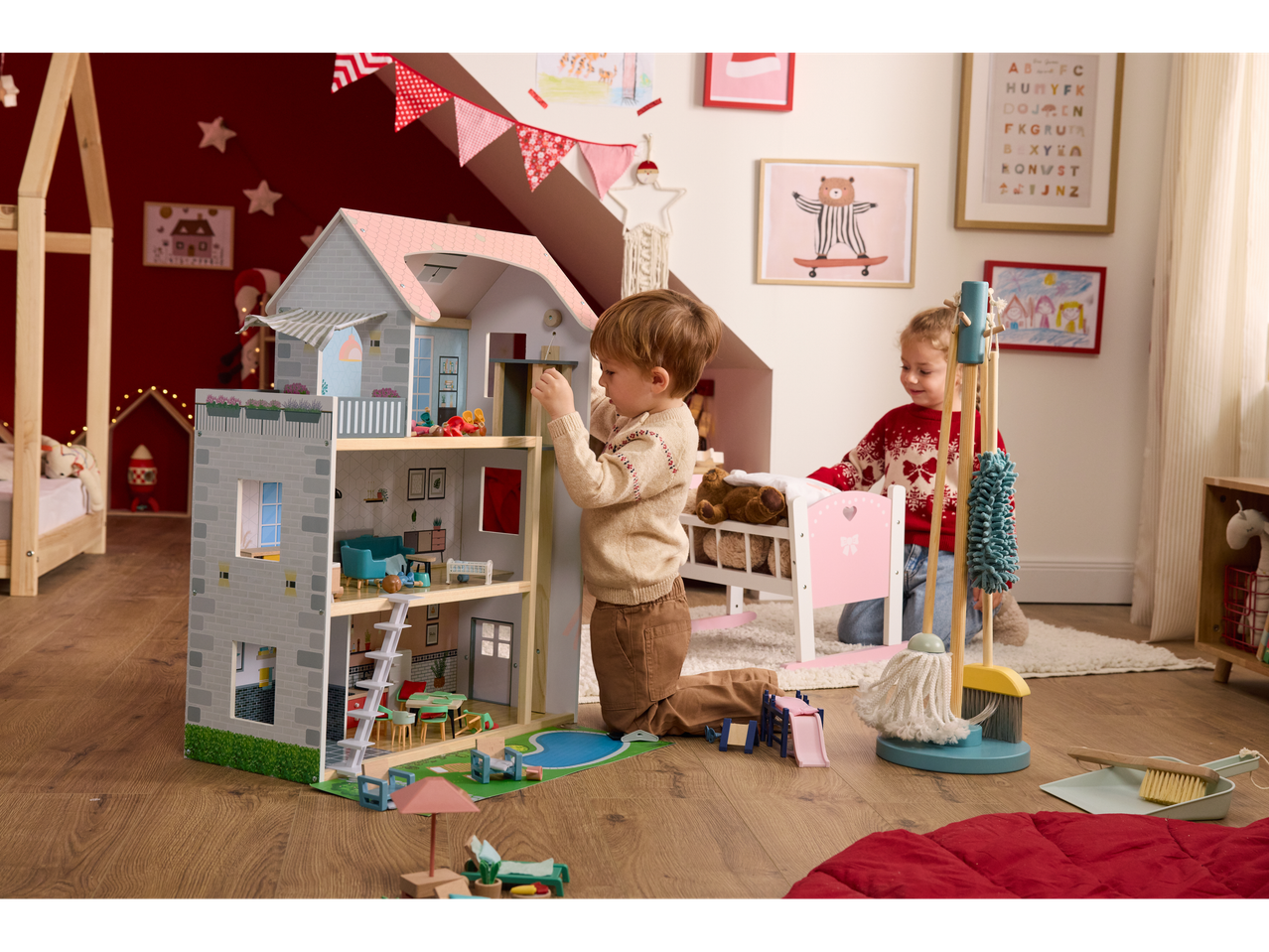 Two children playing with a wooden doll's house and furniture set.