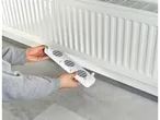Hands holding a white SILVERCREST® Radiator Booster with three fans, positioned near a white radiator.