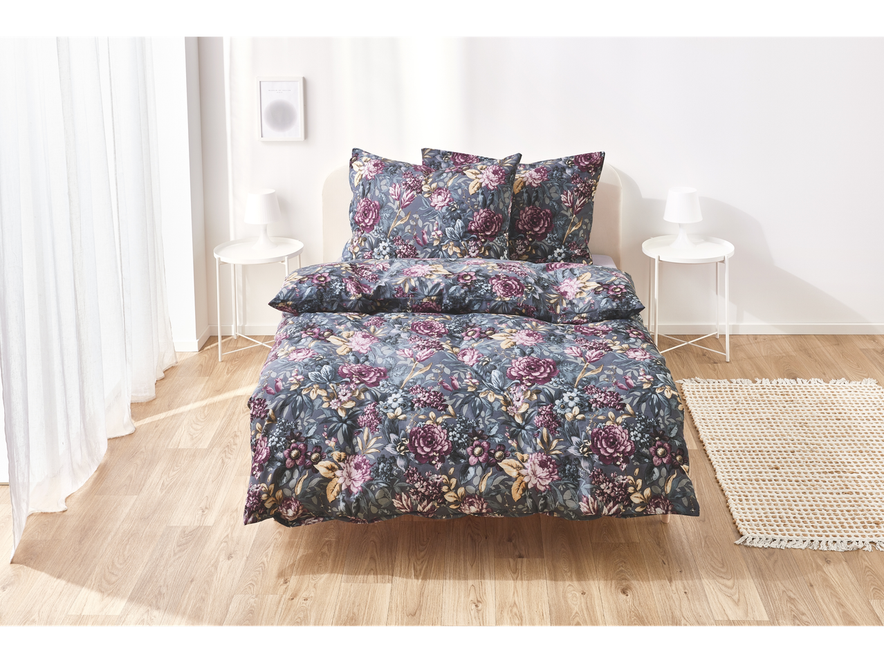A floral duvet cover set in dark grey tones adorns a bed in a bright bedroom.