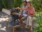 Couple grilling on a kamado barbecue, preparing food on a patio.