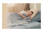 A woman sleeping peacefully under a grey quilted weighted blanket in a cozy bedroom.