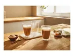 Two double-walled glasses with coffee, one empty, on a wooden table with macarons and sugar.