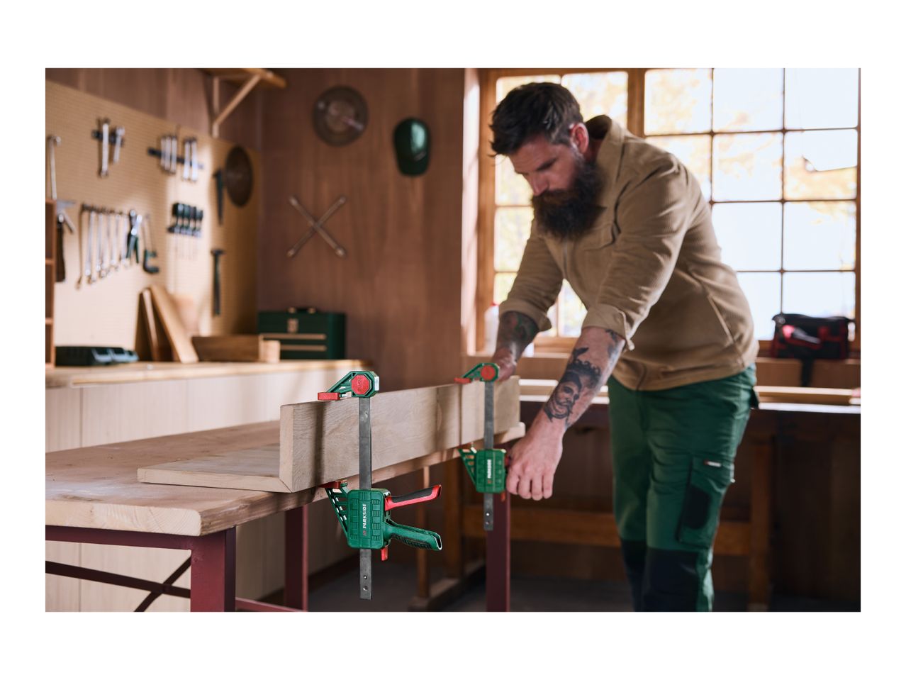 Man in a workshop using bar clamps to secure a wooden board on a workbench.