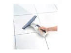 A hand holding a window vacuum cleaner, cleaning a white tiled surface, leaving a streak of clean.