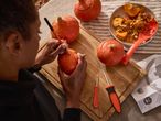 A person carving a pumpkin with a marker, surrounded by other pumpkins and carving tools.