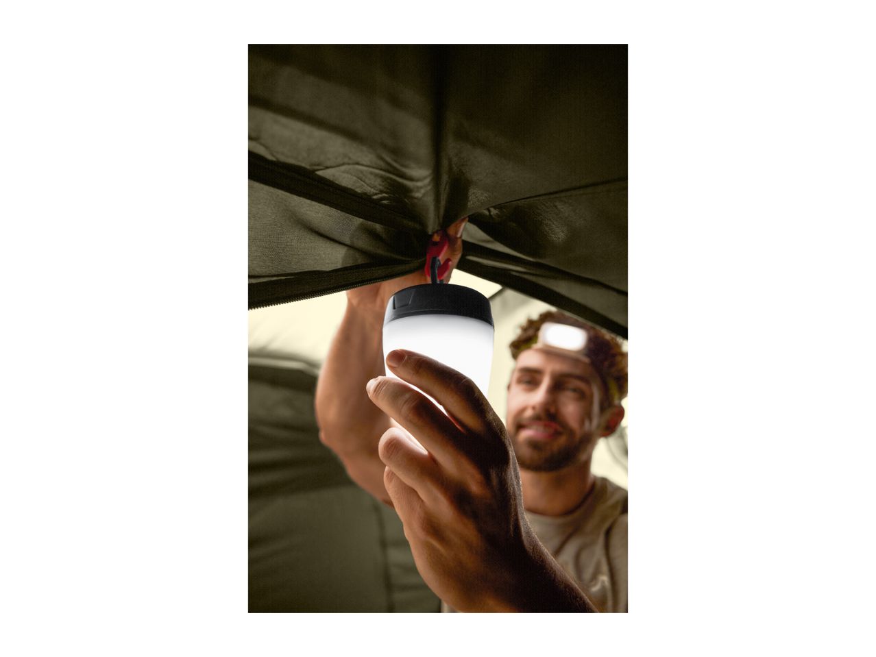 Man hanging a camping lantern inside a tent, wearing a headlamp.