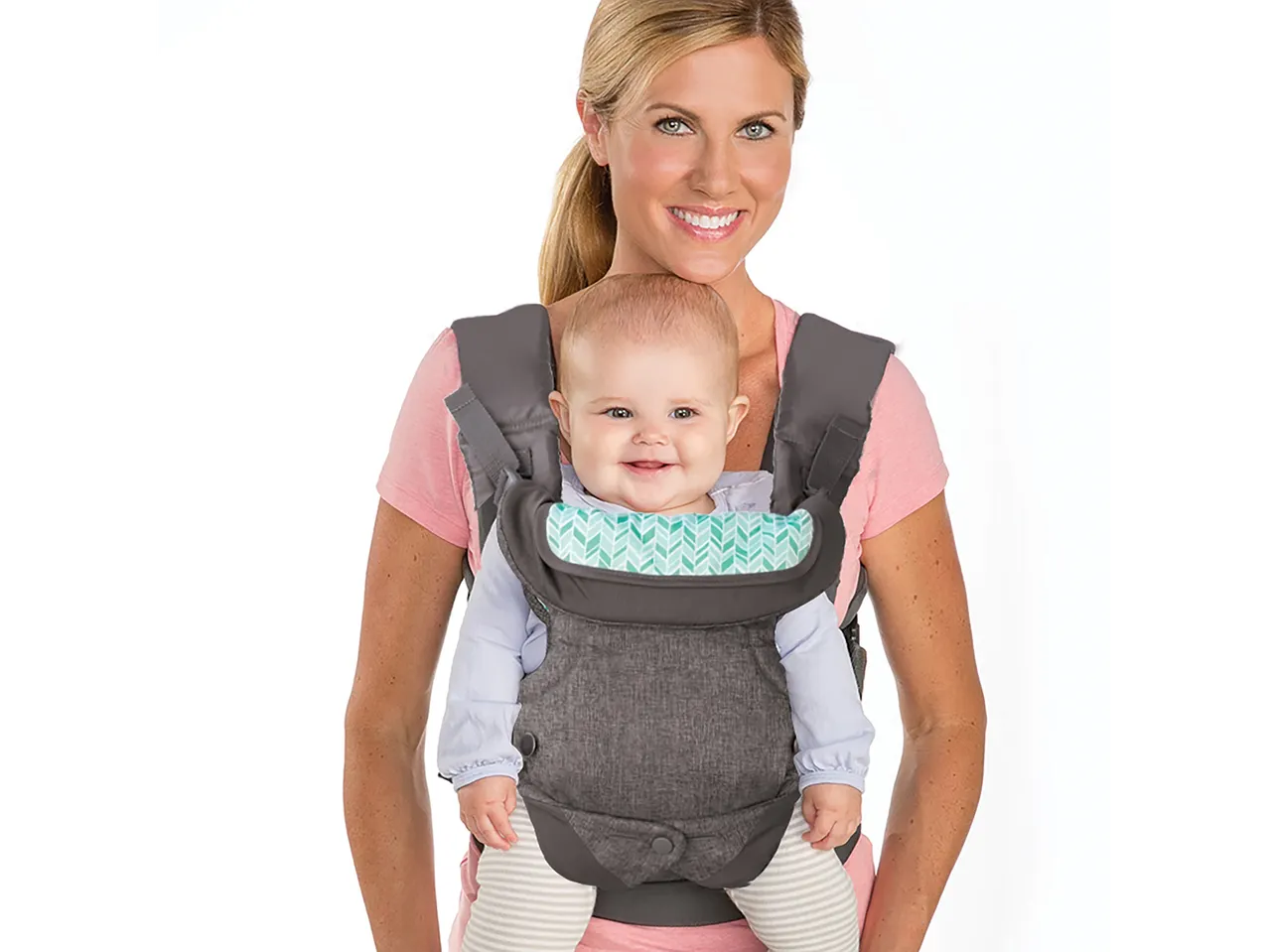 A woman smiles while carrying a baby in a gray baby carrier.