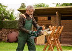 A man in overalls and safety gear uses a PARKSIDE® 20V Cordless Chainsaw to cut logs on a wooden sawhorse.