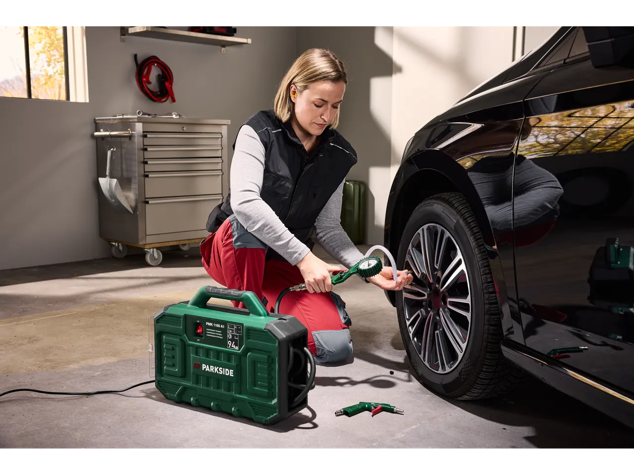 Woman using a Parkside® Portable Compressor to inflate a car tire in a garage.