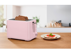 Torradeira rosa com torradas e uma sanduíche aberta numa mesa de madeira.