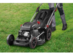 Person in work trousers pushing a black lawnmower with red accents on green grass.