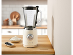 A vintage-style blender on a wooden counter with blueberries and cream.