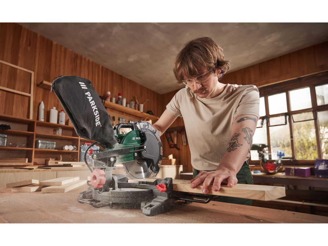 A man uses a Parkside miter saw to cut a piece of wood in his workshop.