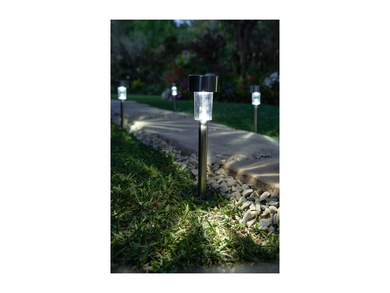 Solar path lights illuminating a garden walkway at dusk.