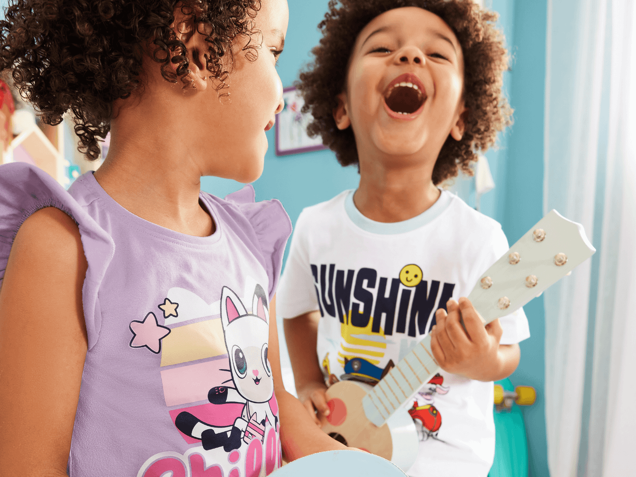 Zwei Kinder spielen mit Musikspielzeug; eines trägt ein Shirt mit Sunshine-Motiv.