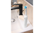 White electric toothbrush with blue bristles on a bathroom sink next to a black faucet.
