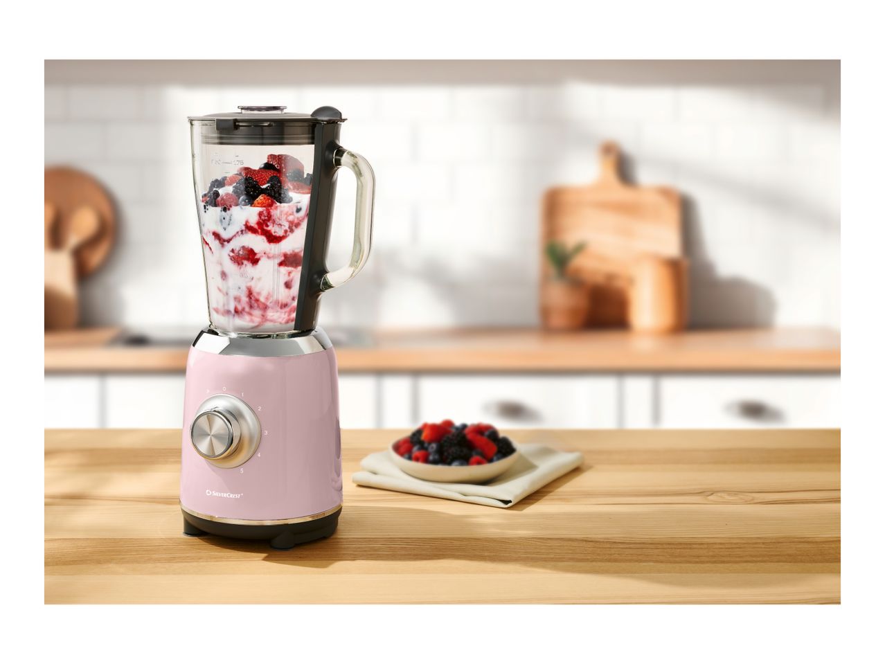 Pink SilverCrest blender with berries and yogurt on a wooden kitchen counter.