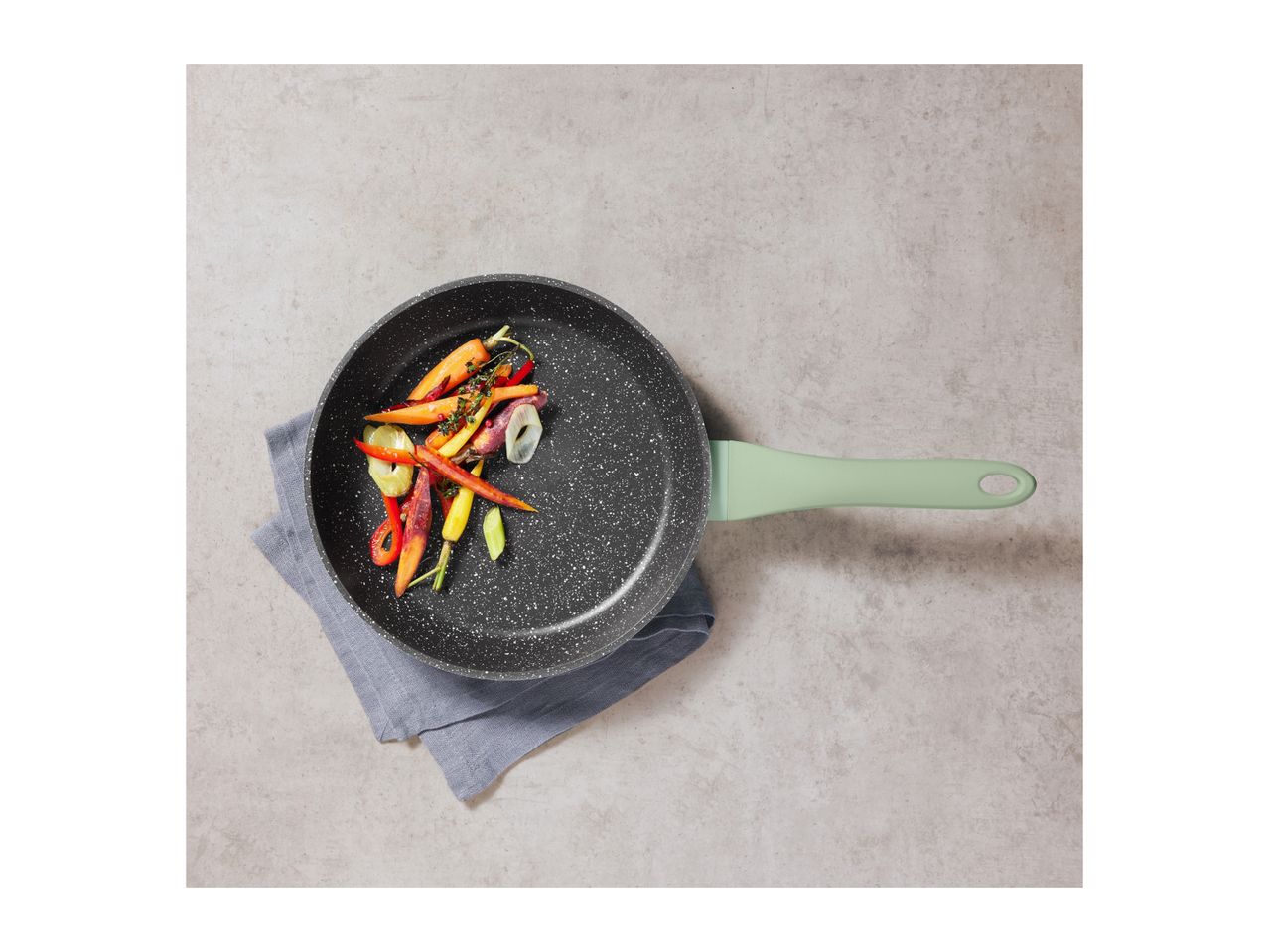 Frying pan with a light green handle, filled with colorful vegetables, on a grey background.