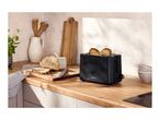 Black toaster with two slices of toast, bread, and kitchen utensils on a wooden counter.