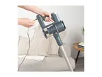 Person plugging in a cordless stick vacuum cleaner on a sofa.