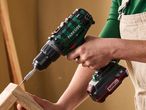 A person using a cordless drill to screw into a piece of wood.