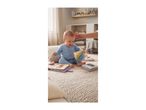 Happy baby in blue sleepsuit playing with soft toys and fabric books on a textured rug.