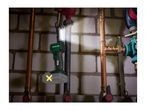 Cordless work light illuminating pipes and a brick wall in a basement setting.