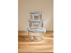 Stack of three round glass food storage containers with blue-rimmed clear lids on a wooden surface.
