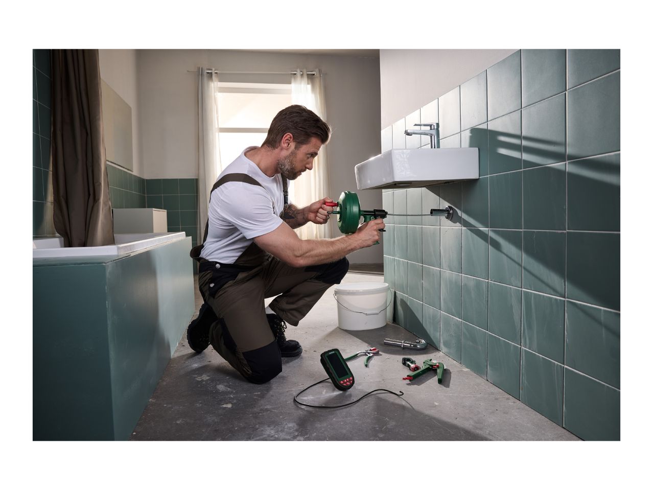 Man using a drain cleaning tool to unclog a sink in a bathroom, with other tools nearby.