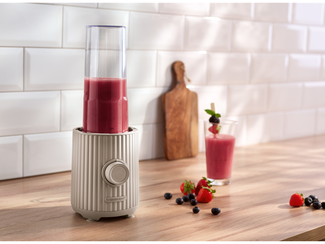 SILVERCREST® To Go Smoothie Maker blending a red smoothie on a wooden counter with berries.