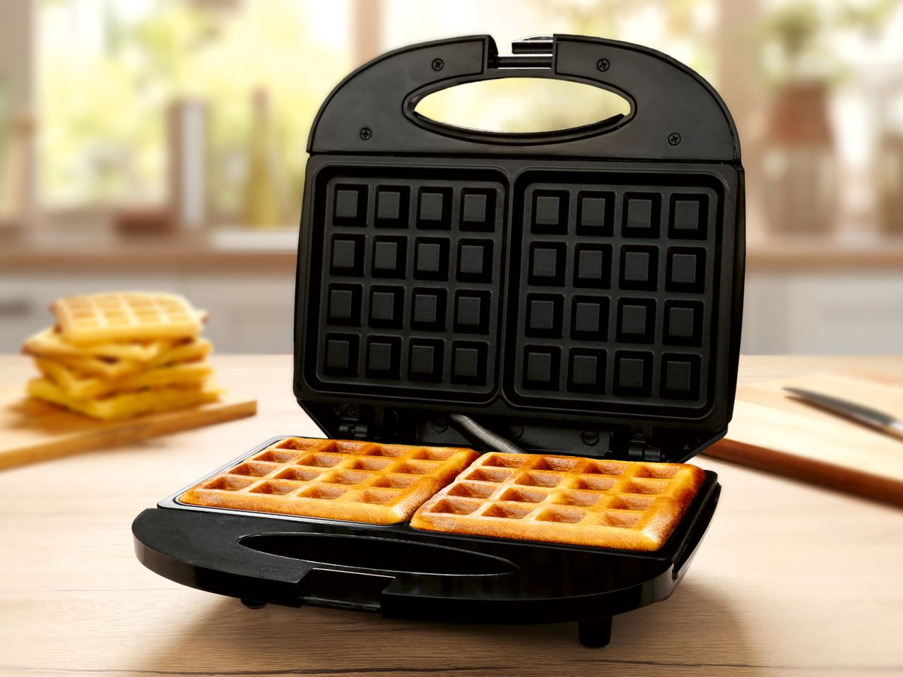 A black double waffle maker with two golden waffles cooking inside.