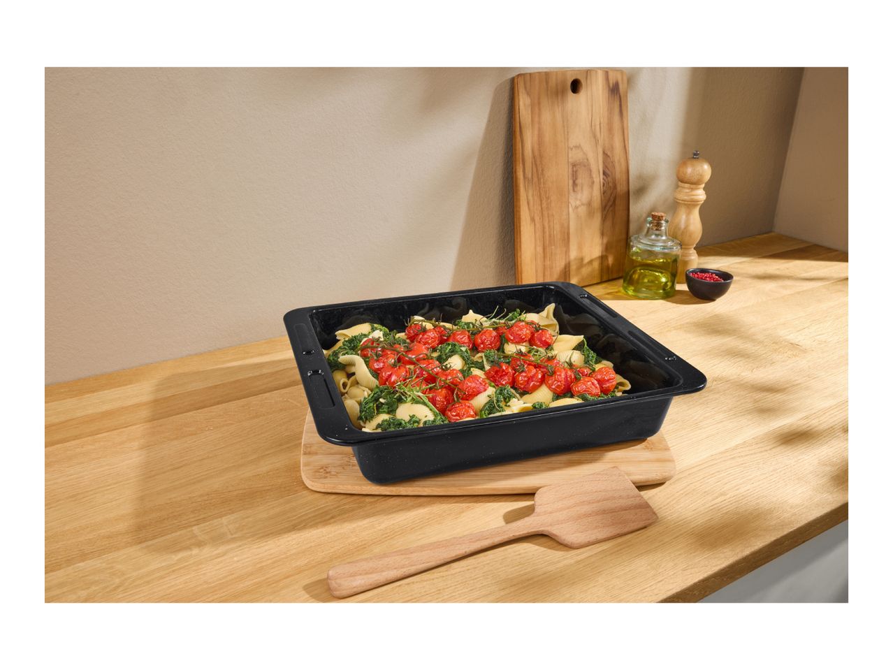 Pasta bake with tomatoes and spinach in a black baking dish on a wooden counter.