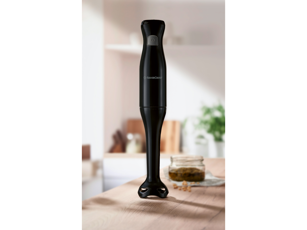 A SilverCrest black hand blender stands on a wooden counter in a kitchen setting.