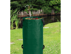 A green garden waste bag filled with autumn leaves sits on a grassy lawn near a pond.