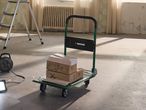 Hand truck with boxes of tiles and a power reel in a room under renovation.