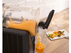 Mașină neagră de granita turnând granita de piersici într-un pahar, cu piersici tăiate în fundal.