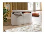Cream boucle storage ottoman with a blanket and pillows, on a wooden floor.