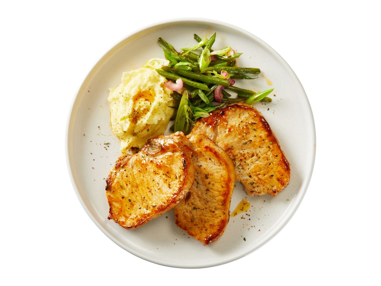 Pan-seared pork chops served with mashed potatoes and green beans.