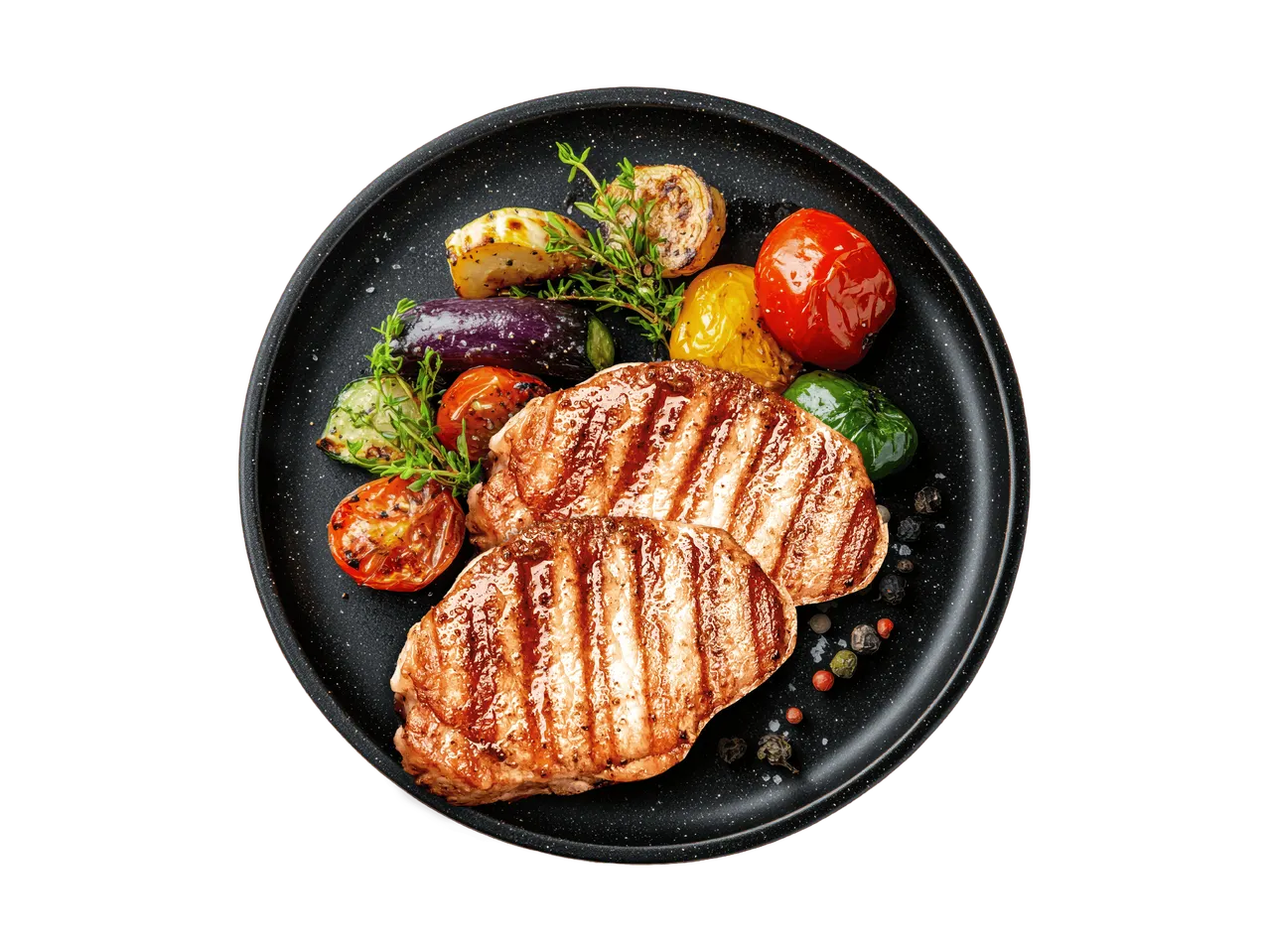 Gegrillte Schweinekoteletts mit gegrilltem Gemüse auf einem schwarzen Teller.