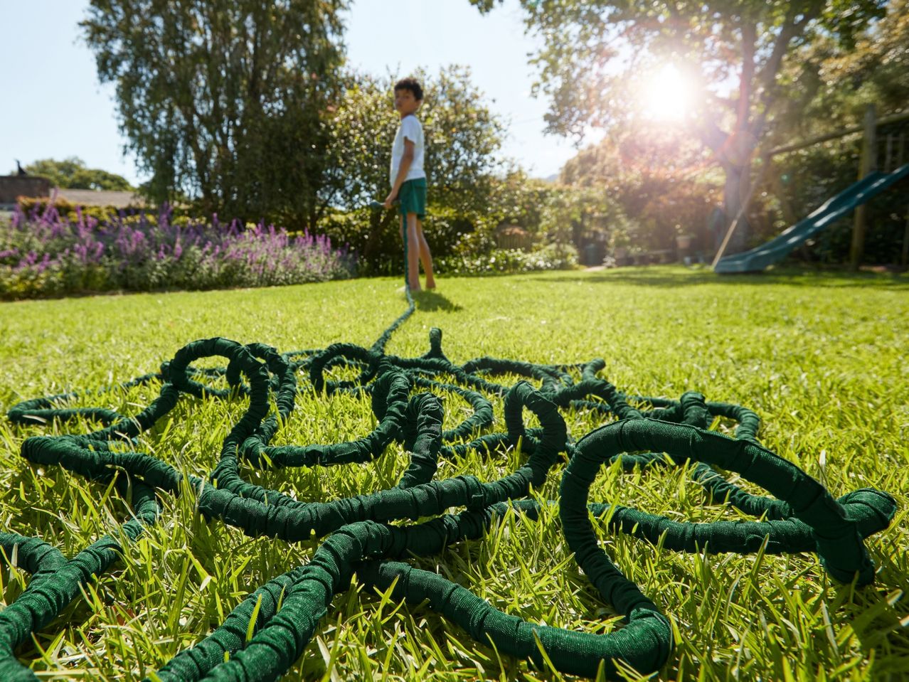 A green garden hose lies coiled on a lush lawn.