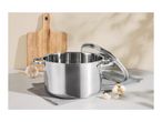 Stainless steel cooking pot with lid, garlic, and wooden cutting board on a kitchen counter.