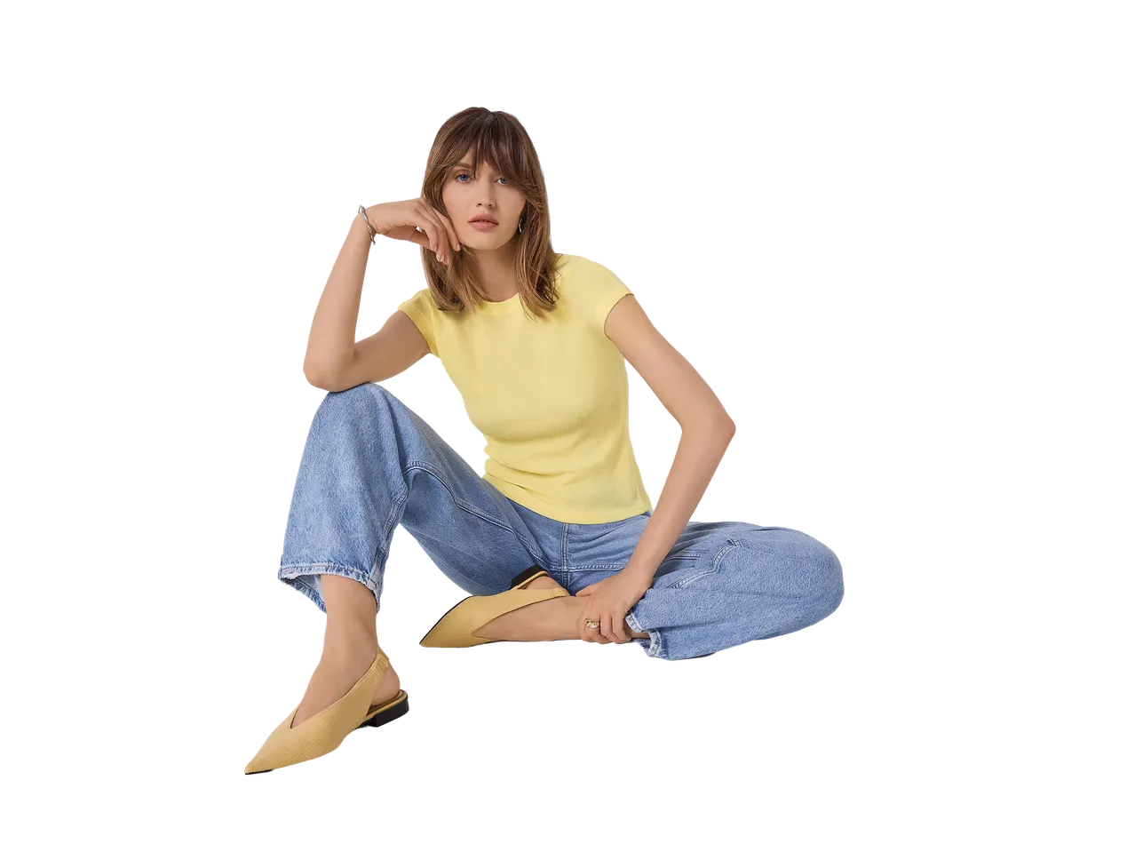 Nő sárga pólóban, kék farmerben és sárga cipőben ülve.
