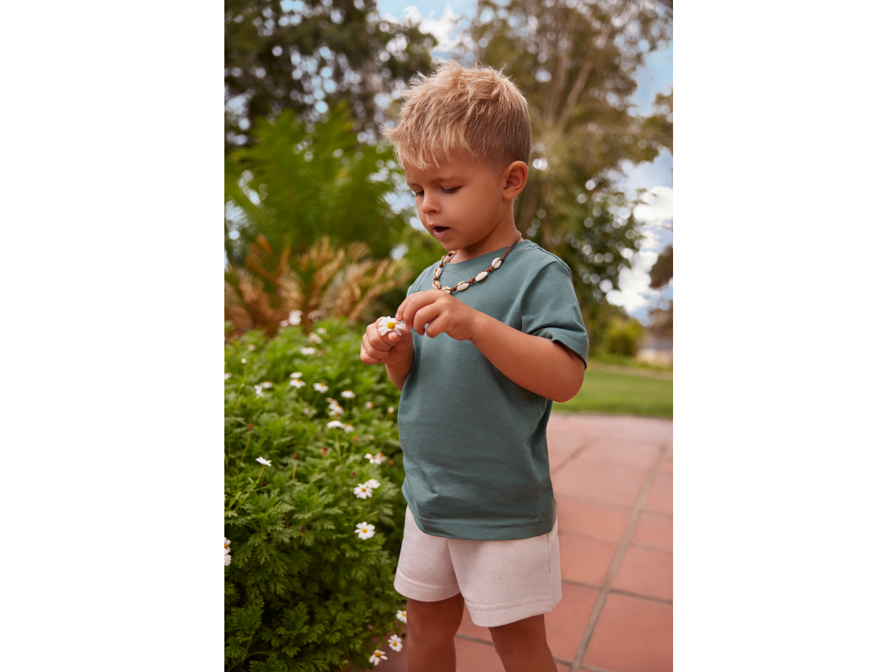 Lupilu boy in green T-shirt and shorts, holding a daisy.