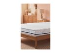 White mattress topper on a wooden bed frame in a bedroom with a rattan cabinet and lamps.