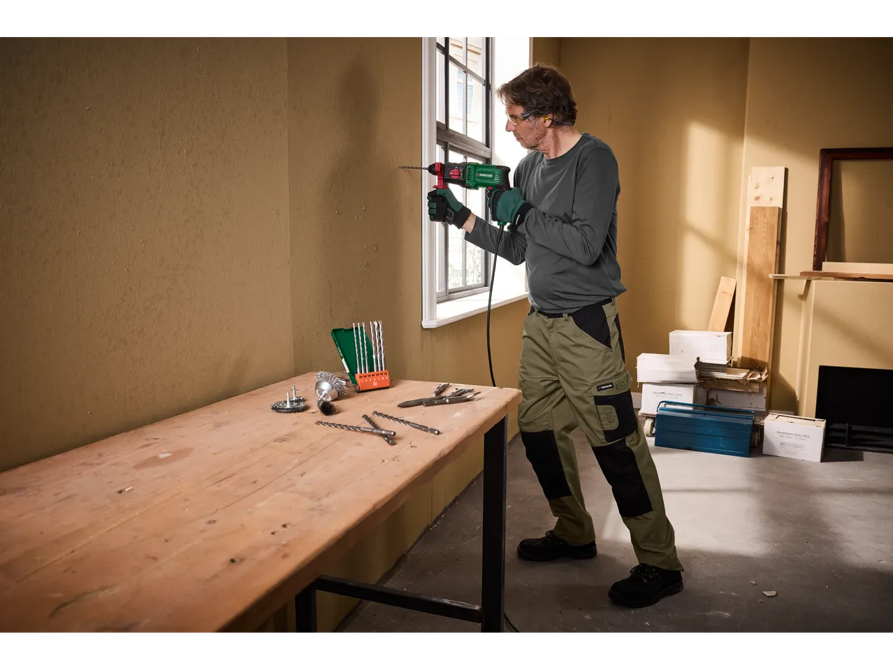 Man drilling into wall with Parkside rotary hammer, tools on table.