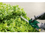 Trimmer de gard viu PARKSIDE tăind un tufiș verde.