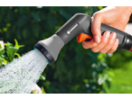 Mão segurando uma pistola de rega GARDENA, pulverizando água contra um fundo verde.