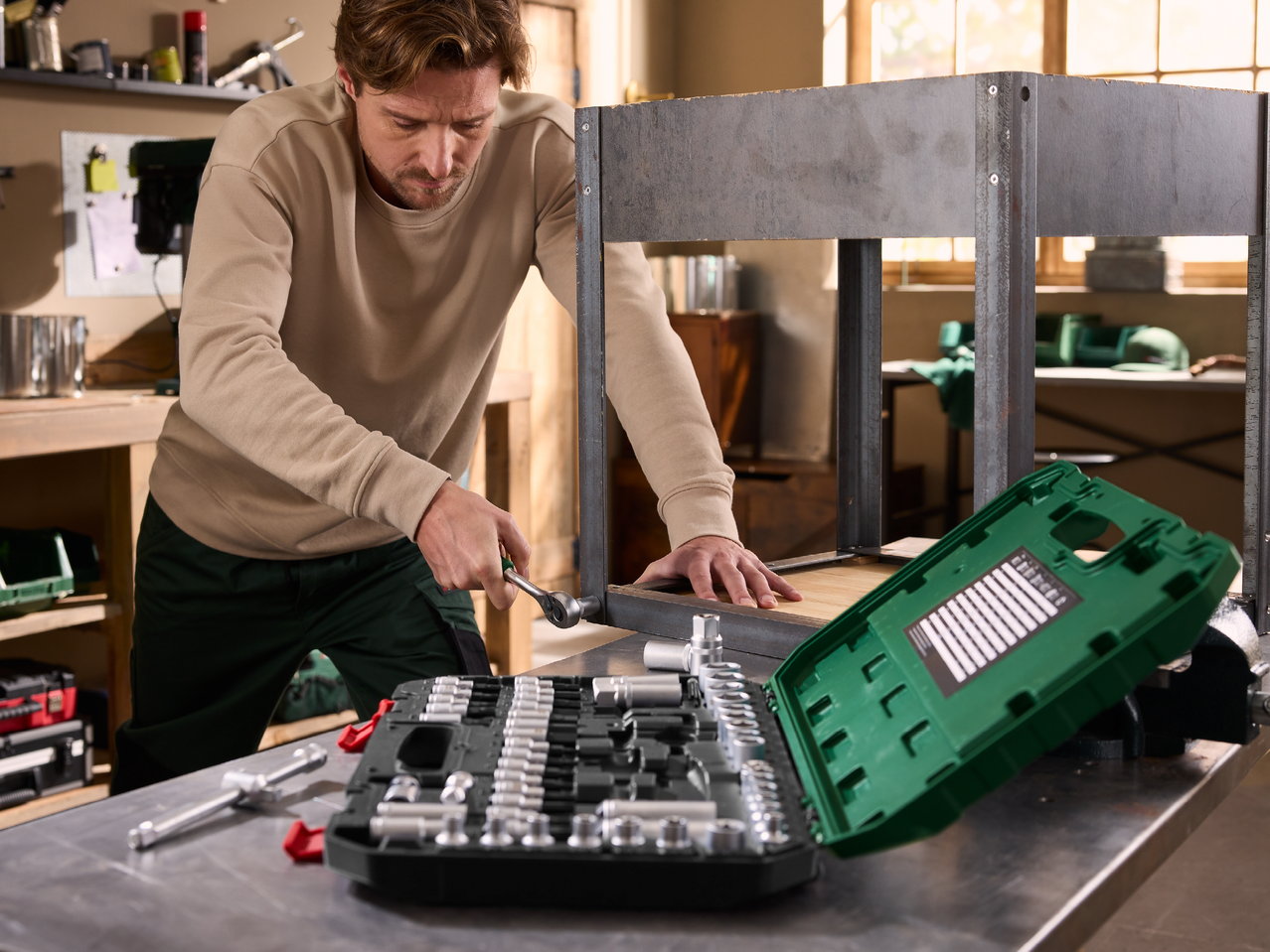 Мъж с комплект инструменти сглобява метална рамка на работна маса.