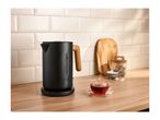 Black kettle with wooden handle on a kitchen counter with a cup of tea.