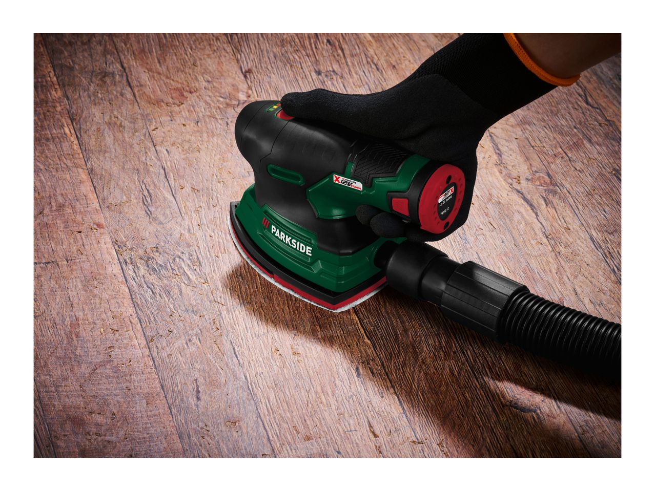 A person sanding a wooden floor with a power sander connected to a dust extraction hose.